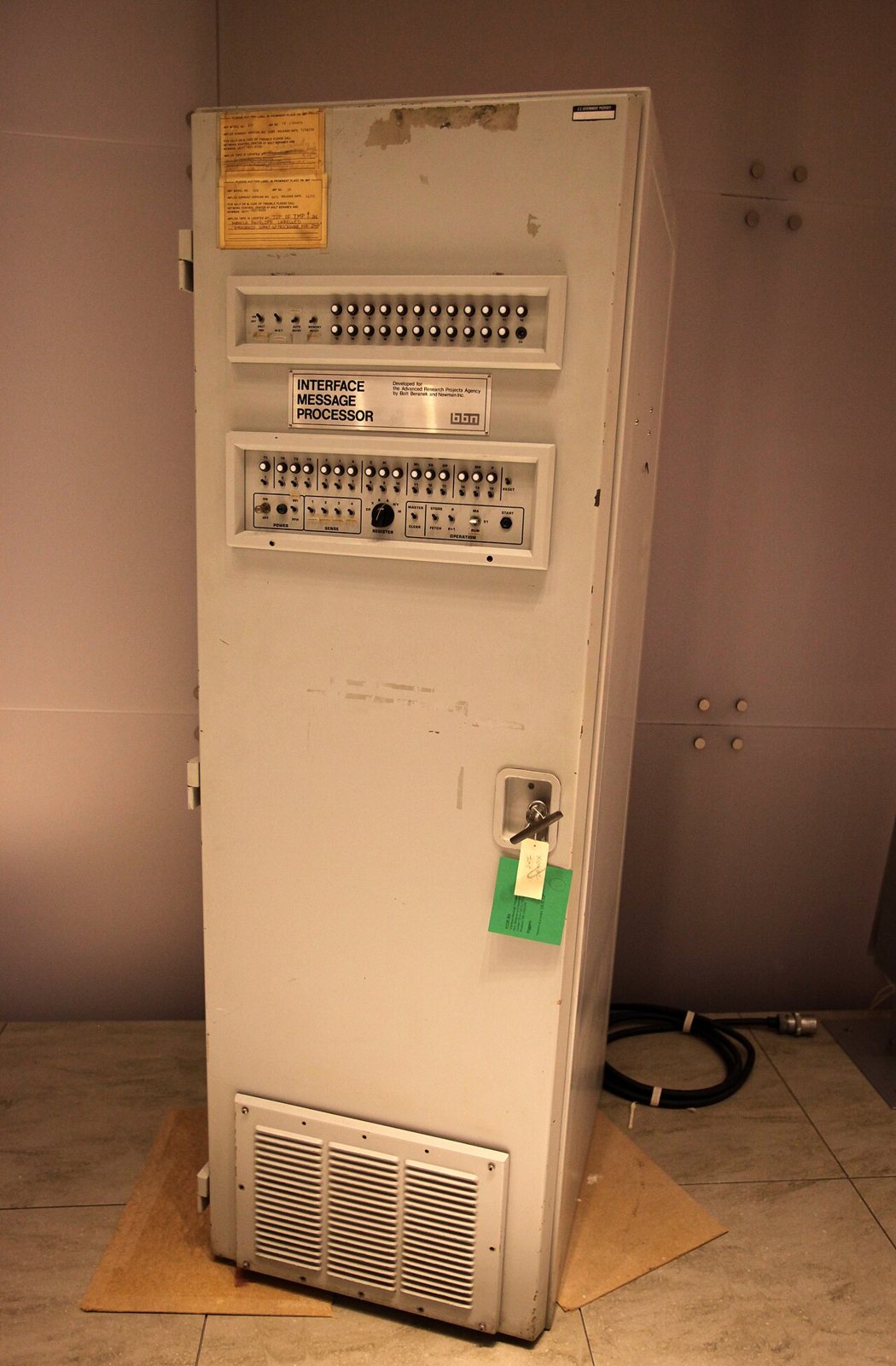 A tall beige BBN Interface Message Processor cabinet with rows of switches and a nameplate on its front panel