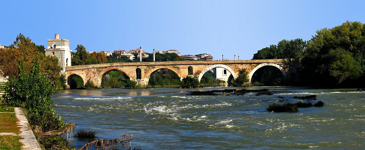 The stone arches of the Ponte Milvio crossing the fast-flowing Tiber in Rome under a clear blue sky